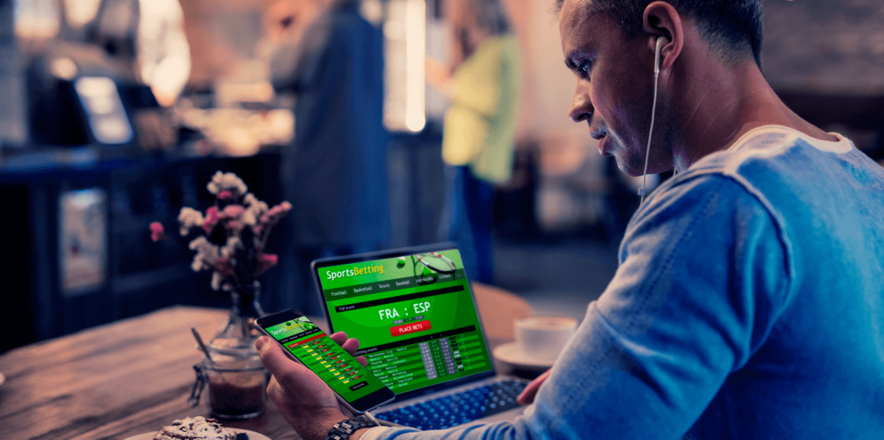 Homem com computador e celular ligado para realizar pagamentos de apostas online.