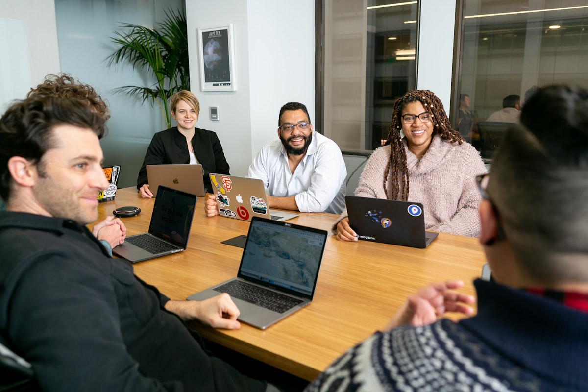 Equipe de tecnologia em reunião de estratégia, todos com laptops abertos, ouvindo apresentação sobre priorização de projetos