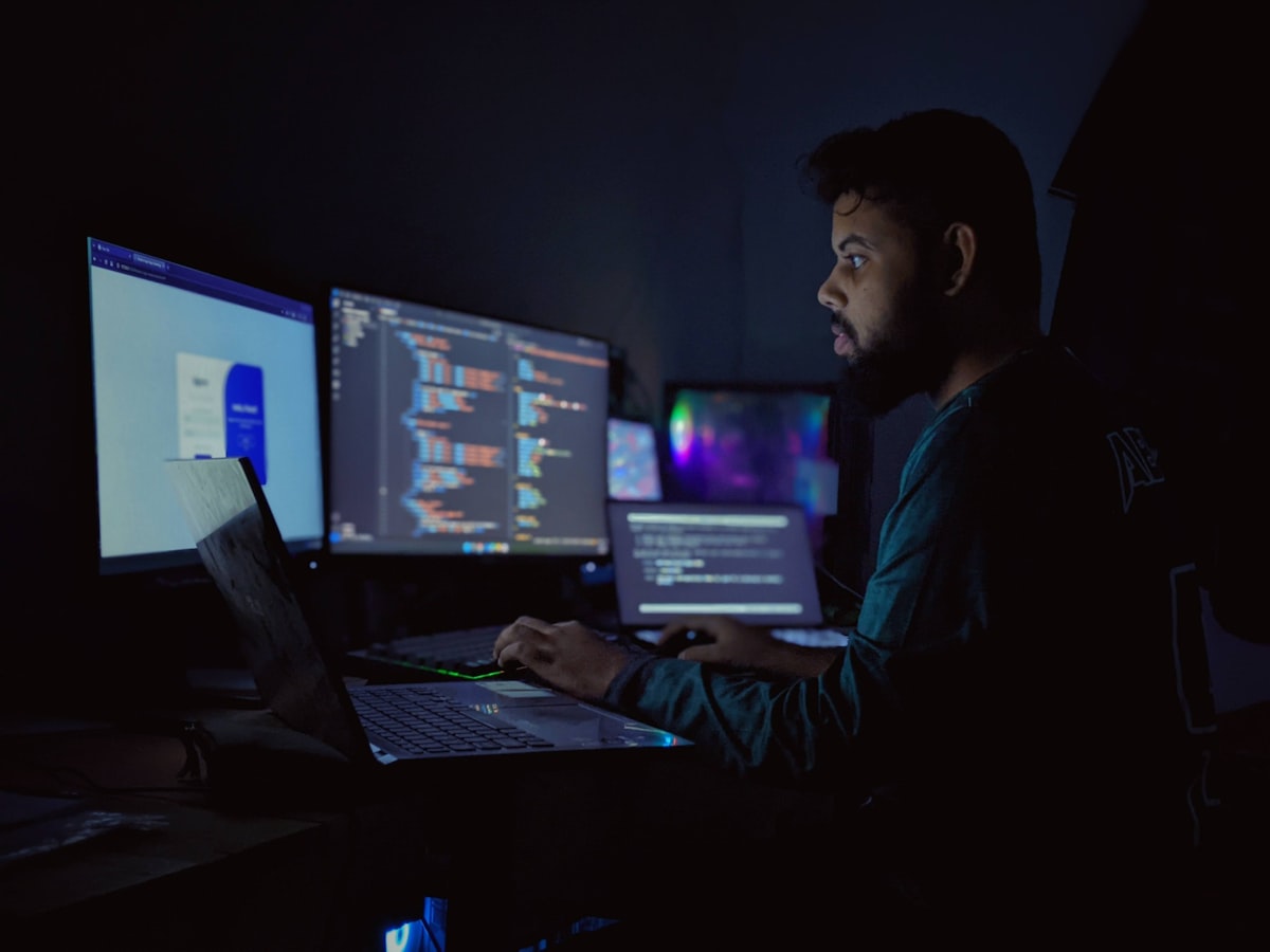 Desenvolvedor programando à noite em ambiente com múltiplos monitores exibindo código